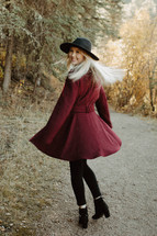 a young woman in a maroon coat and hat standing outdoors 