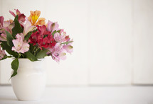 colorful flowers in a vase with a white wood background.