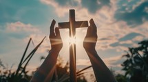 Silhouette of hands and a cross on sunset sky background