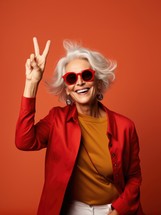 Portrait of smiling senior woman in sunglasses showing peace sign isolated on orange
