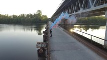 Young woman stands on a bridge. The girl comes to the edge of the bridge. with color smoke