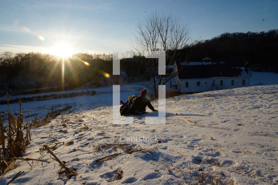 kids sledding down a hill at sunset 
