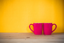 red coffee mugs against a yellow background 