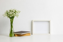vase of white flowers and books with blank frame 