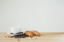 coffee beans, cup and saucer, and croissants on wood countertop 