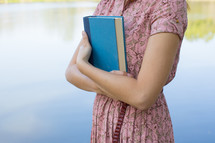 torso of a young woman in a pink dress holding a Bible 