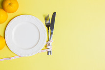 Diet concept with spoon, knife, oranges and clock over the yellow background. 