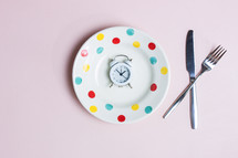 Eating healthy concept with clock, knife and fork over the pink background.