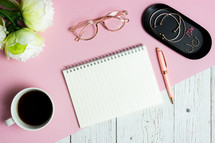 Women working items with notebook, coffee cup, glasses and roses over pink and wooden table. 