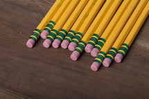 A row of yellow wooden pencils on a wooden surface.