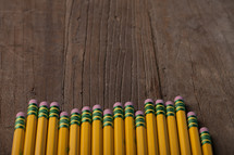 A row of yellow pencils with pink erasers on a wooden surface.