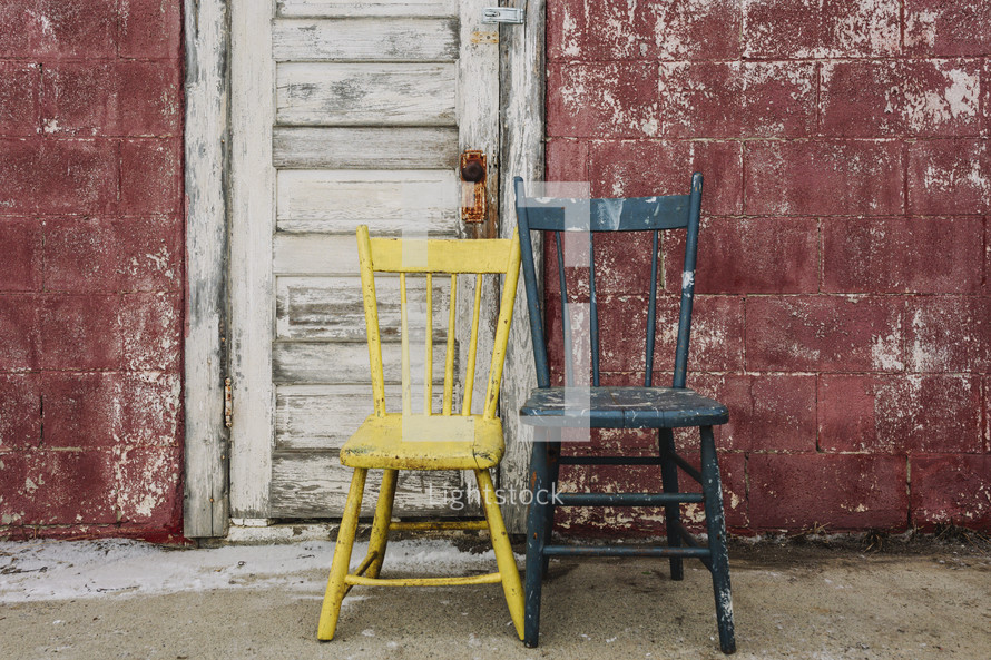 two old chairs standing empty against a rustic red wall background 