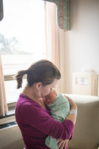 A woman holds a newborn baby in a hospital room.