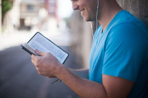 man reading a Bible and listening to earbuds 