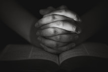 Person with hands clasped in prayer on open Bible