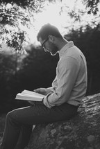 man reading a Bible outdoors sitting on a rock 