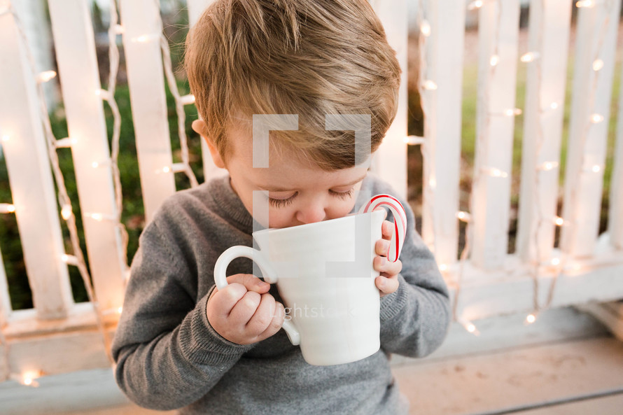child holding a mug of hot cocoa with a candy cane 