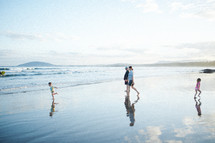 a family walking on wet sand at the beach 