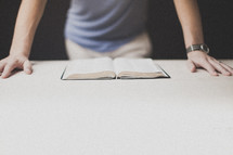 Man's hands leaning on a table with am open Bible.