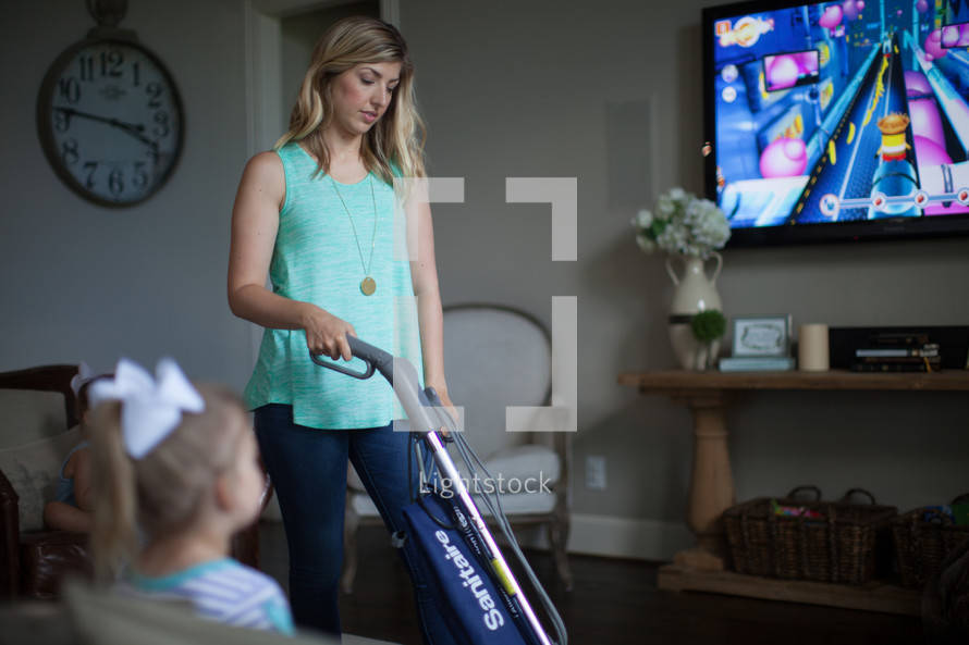 a mother vacuuming while child watches tv 