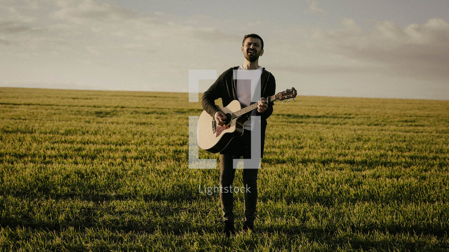 a man standing in a field playing a guitar 