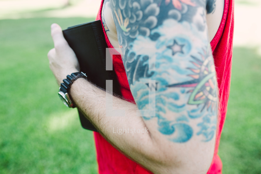 man with a sleeve tattoo holding a Bible 
