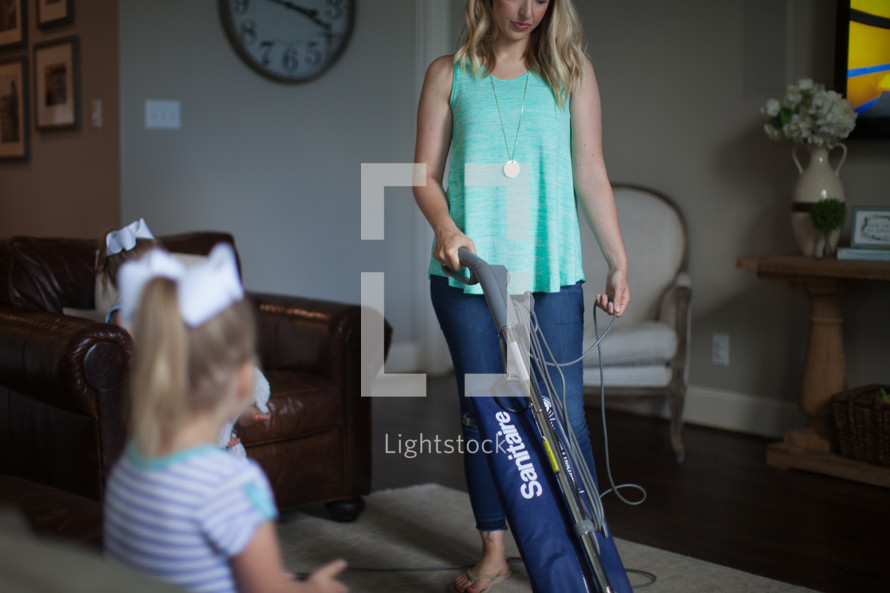 a mother vacuuming while daughter watches tv 