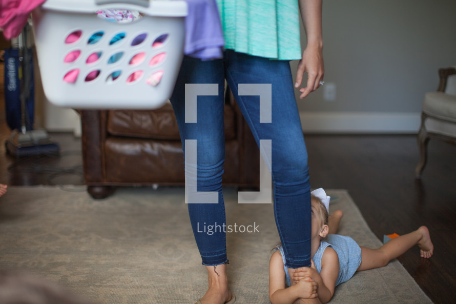 a mother with a laundry basket and daughter hanging on to her leg