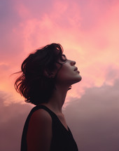 A young woman looking with eyes closed head lifted toward sky during sunset
