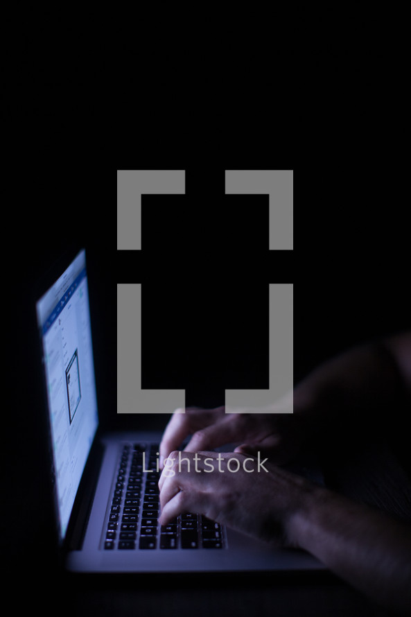 a man typing and looking at a computer screen at night 