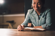Smiling woman reading the Bible at a table.