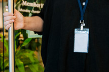 Woman in a black shirt wearing a lanyard while holding a door open.