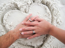 hands of a married couple on a heart drawn in the sand 