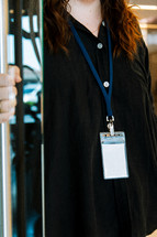 Woman in a black shirt wearing a lanyard while holding a door open.