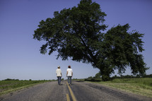 two men standing in the middle of a road with their backs to the camera 