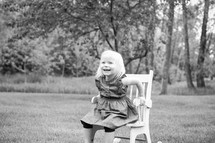 a little girl sitting in a chair outdoors