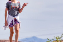 a little girl wearing a love t-shirt standing on a mountaintop pointing to the side 