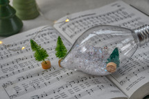 snow in bulb ornament and miniature Christmas trees on a hymnal for Christmas worship service music 