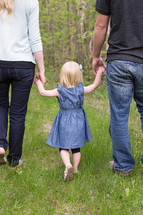 mother, father, and daughter walking outdoors holding hands 