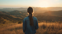 A girl looking out over hills and a valley during sunset