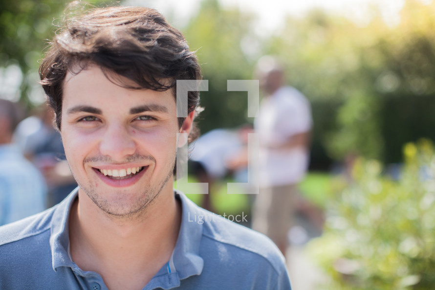 headshot of a young man and friends talking at a backyard summer party
