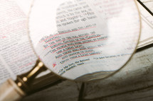 Magnifying glass over pages of Bible open to Matthew 4:15 laying on wooden table.