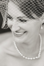 Smiling woman in net veil with pearl necklace and earrings bride wedding 
