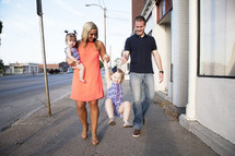 a mother and father walking down a sidewalk with their children 