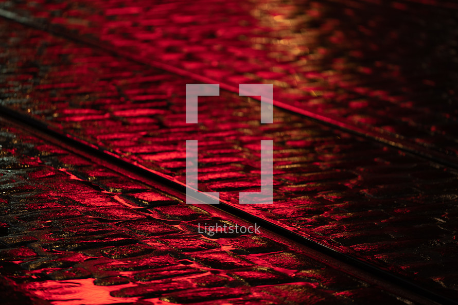 wet cobblestones and tracks glowing red in light at night 