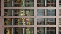 vertical day to night timelapse of people in an office building window 