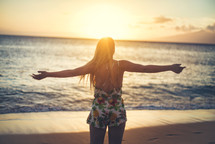 woman standing on a beach at sunset with open arms 