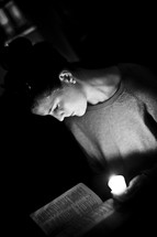 Woman reading Bible by candlelight.
