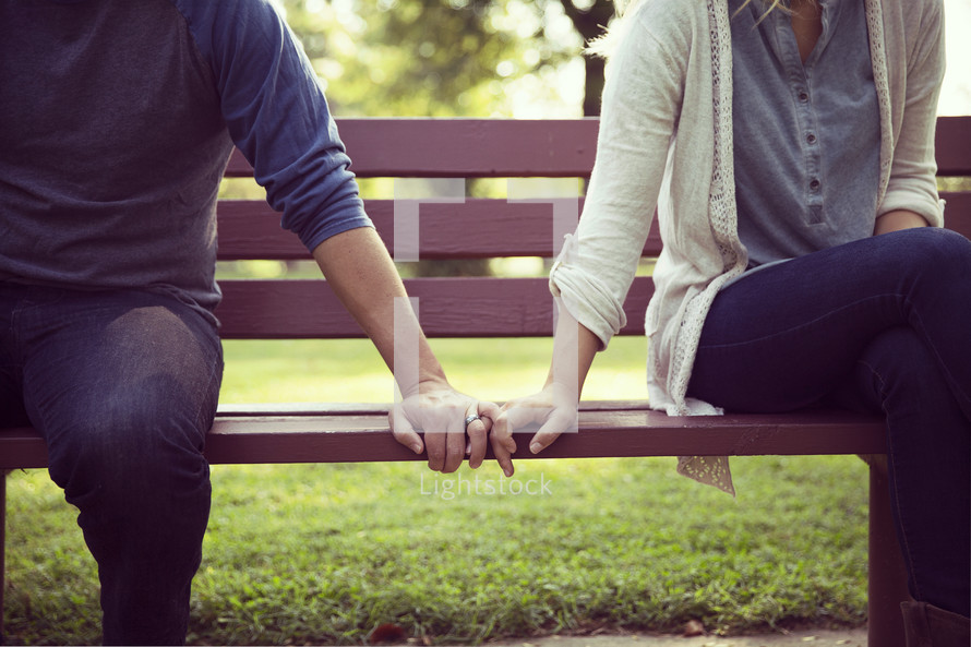 a couple sitting on a bench touching hands 