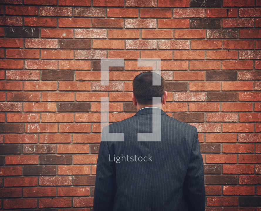 a businessman facing a brick wall 